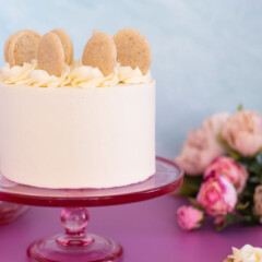 Small cake on a pink cake stand with cookies around.