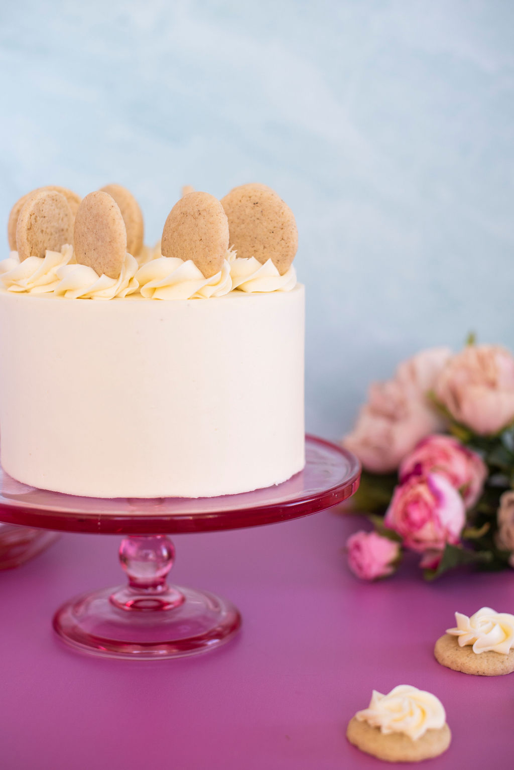 Small cake on a pink cake stand with cookies around.