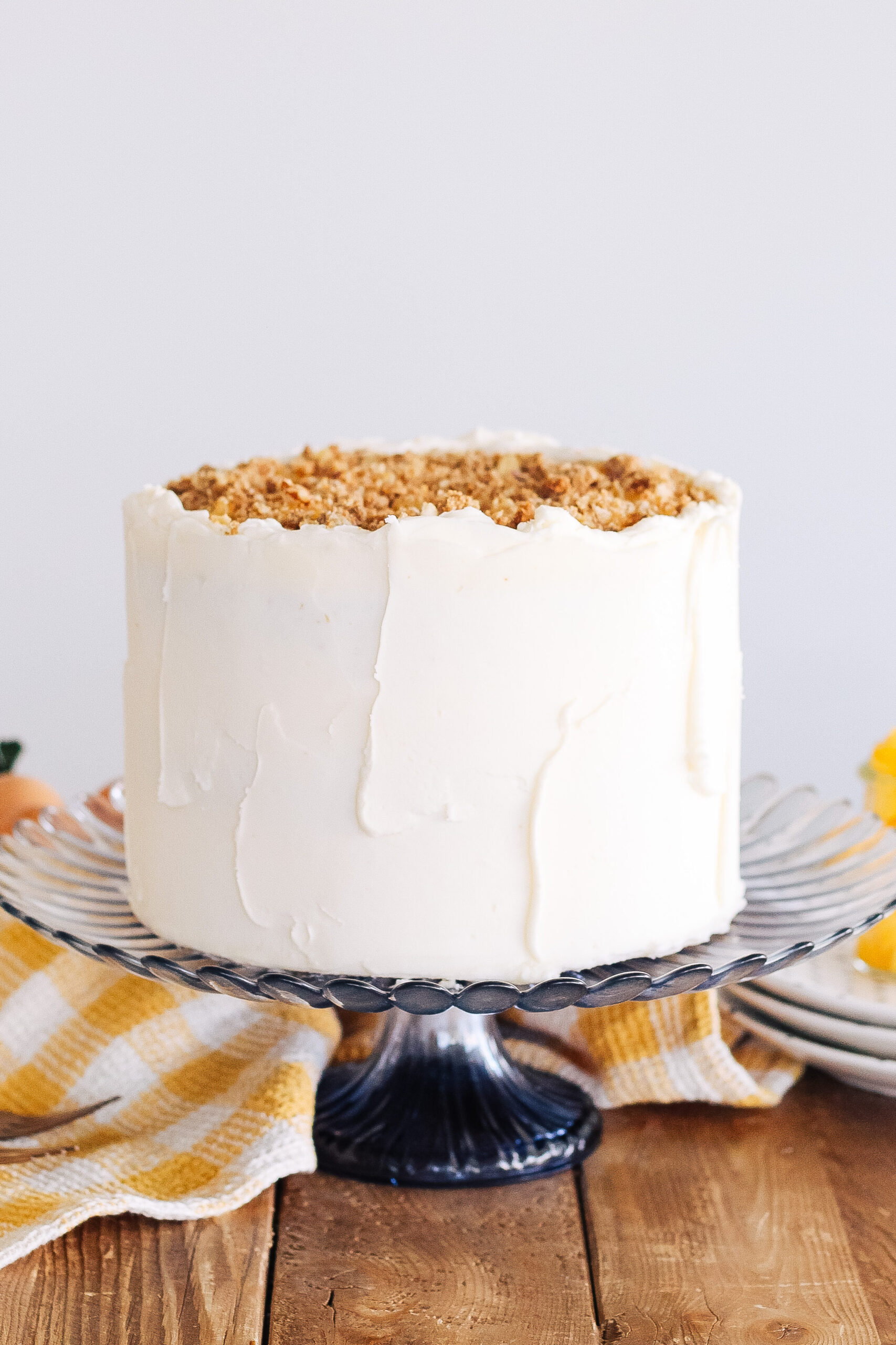 Peach Biscoff Cake on a blue glass cake stand with plates and peaches nearby.