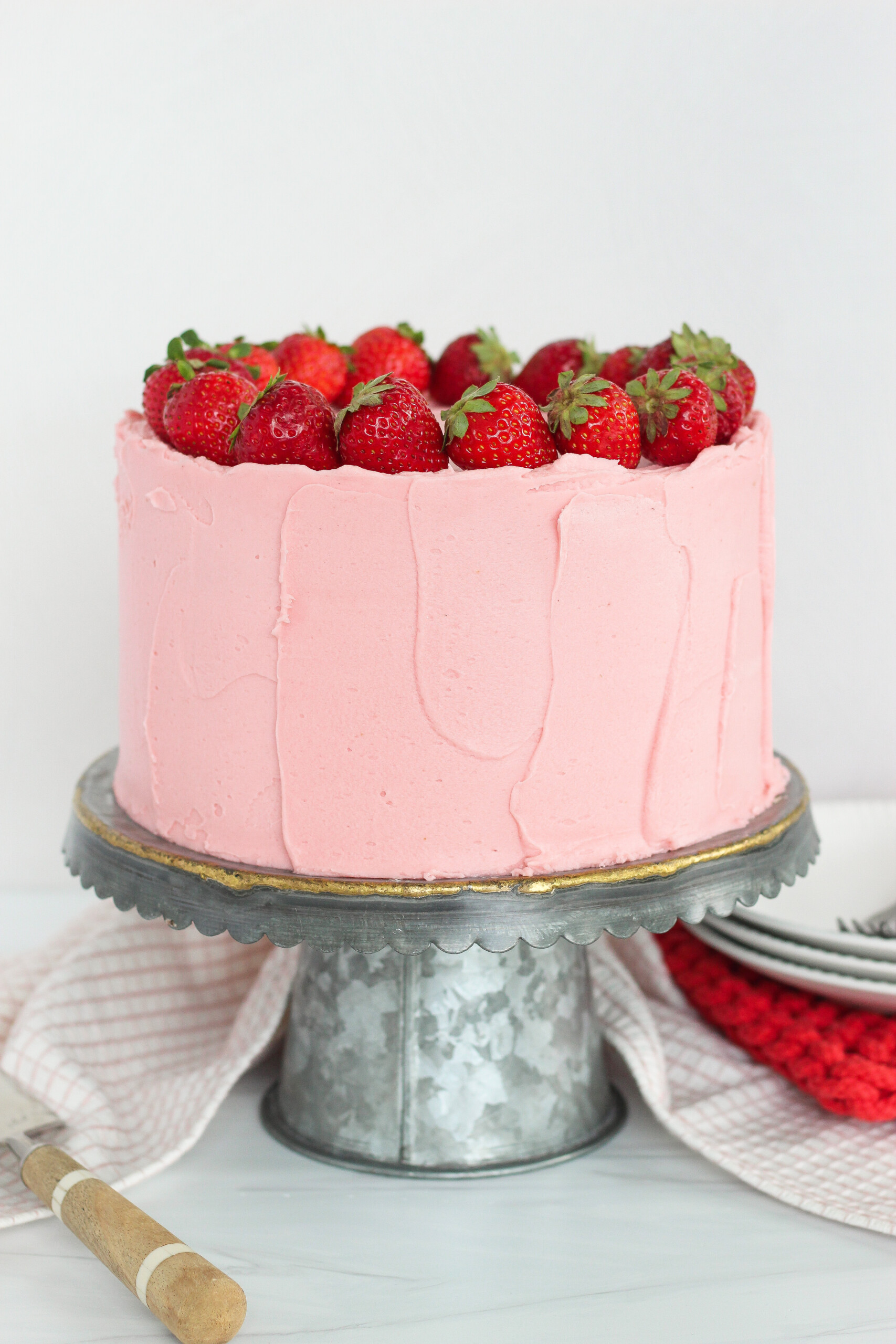 A pink strawberry cheesecake cake on a metal cake stand with plates.